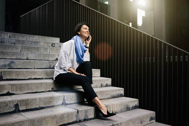 Young woman talking on phone while sitting on the steps at the street - Fotoğraf, Görsel
