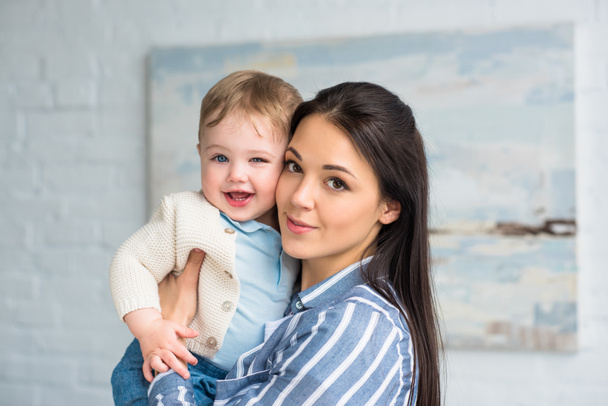 genç anne holding neşeli bebek çocuk elinde evde portresi - Fotoğraf, Görsel