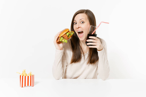Boldog fun fiatal nő ül asztal, hamburger, sült krumpli, cola üvegben elszigetelt fehér background. Megfelelő táplálkozás, vagy a klasszikus amerikai gyorsétterem. Hirdetés terület másol hely. - Fotó, kép