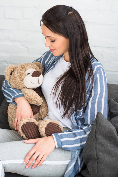 smiling woman with teddy bear resting on sofa at home - Photo, Image