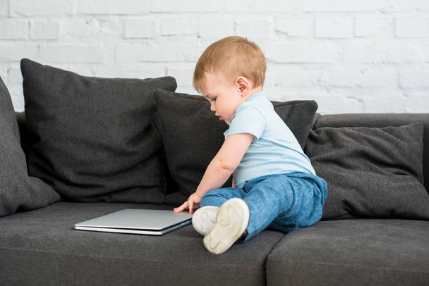 side view of little baby boy with laptop on sofa at home - Фото, зображення
