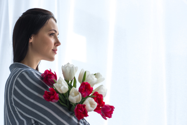 side view of beautiful pensive woman with bouquet of tulips at home - Photo, Image