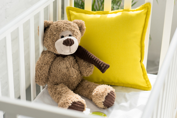 close up view of teddy bear and yellow pillow in baby crib at home - Photo, Image