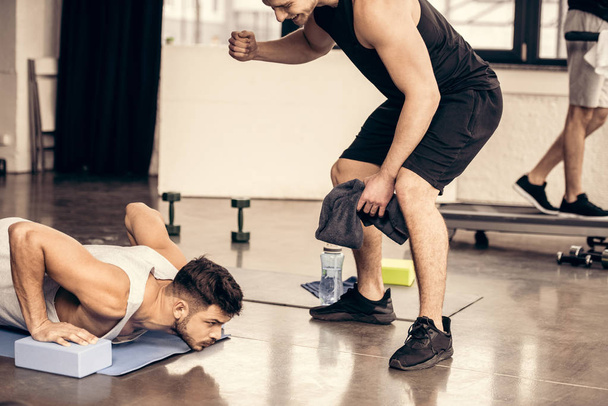 entraîneur soutenant sportif faisant planche sur des blocs de yoga dans la salle de gym
 - Photo, image