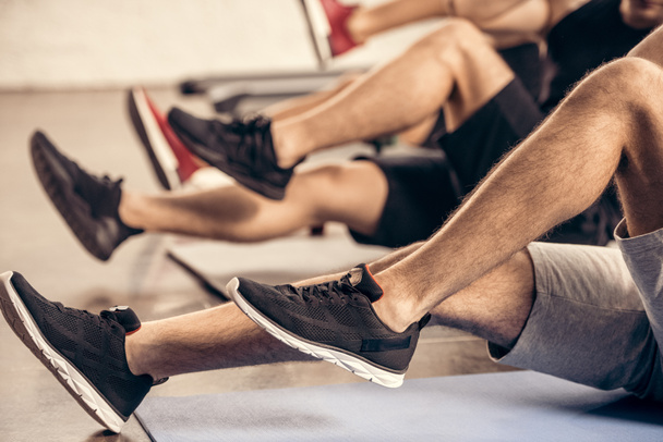 ostřižená fotografie sportovců dělají sit ups společně v tělocvičně - Fotografie, Obrázek