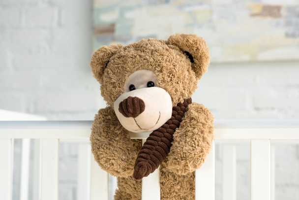 close up view of teddy bear hanging on white wooden baby crib in room - Zdjęcie, obraz