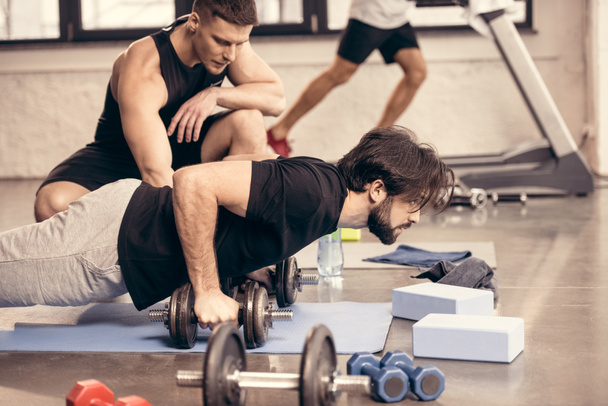 side view of handsome sportsman doing push ups on dumbbells in gym - Foto, Imagem