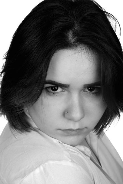 Черно-белый портрет на белом фоне девушки-подростка осуждение эмоций, недовольное выражение лица и сердитые глаза
 - Фото, изображение