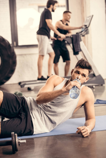 красивий спортсмен п'є воду з пляшки в спортзалі
 - Фото, зображення
