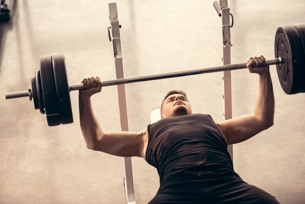 apuesto deportista levantando barra en press de banca en el gimnasio
 - Foto, Imagen
