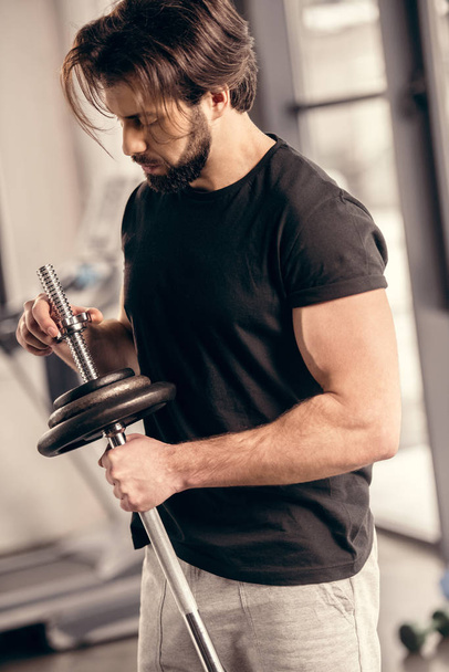 desportista bonito fixação de placas de peso na barra de ferro para treinamento em ginásio
 - Foto, Imagem