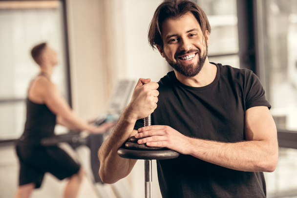 sportif souriant appuyé sur une barre de fer avec des plaques de poids dans la salle de gym
 - Photo, image