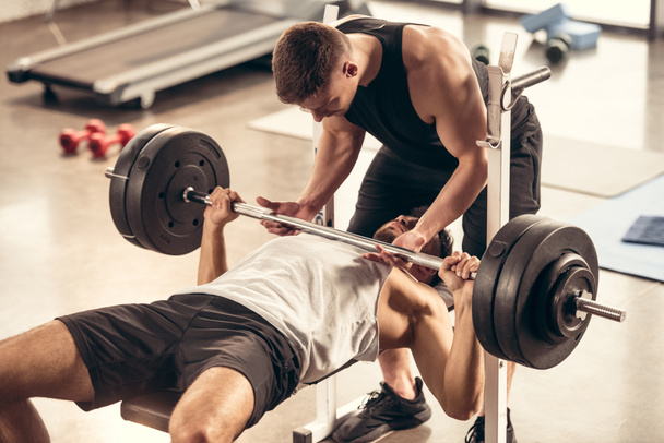 atlétikai edző segít a sportoló emelő nehéz súly lemezek súlyzó edzőteremben - Fotó, kép