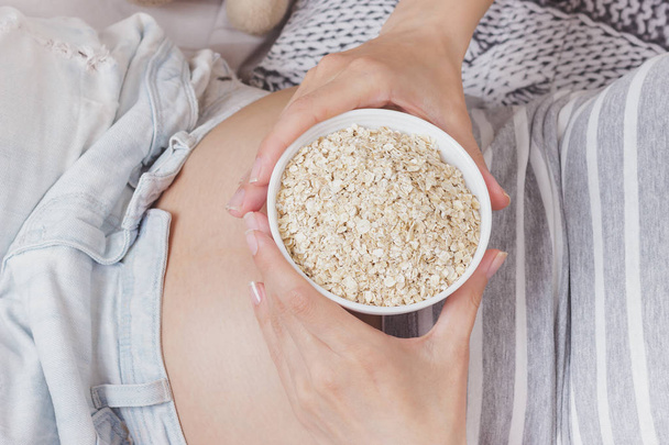 Mujer embarazada con un tazón de avena en el vientre
 - Foto, imagen