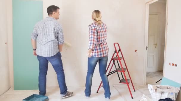Slow motion footage of happy cheerful couple dancing while painting walls with paint roller at their new apartment under renovation - Footage, Video