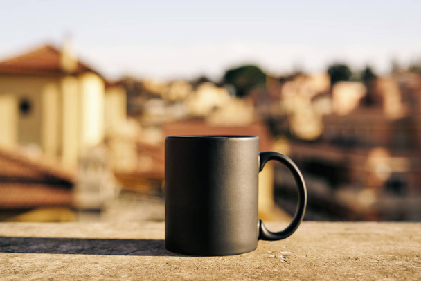 Black cup on a concrete surface with blurred city on background - Фото, зображення