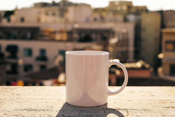 White cup on a concrete surface with blurred city on background - Фото, зображення