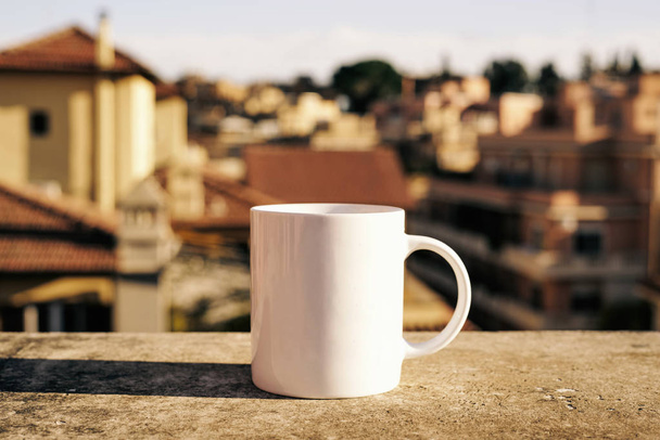 White cup on a concrete surface with blurred city on background - Fotografie, Obrázek