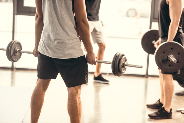 cropped shot of sporty young men in sportswear lifting barbells in gym - Фото, зображення