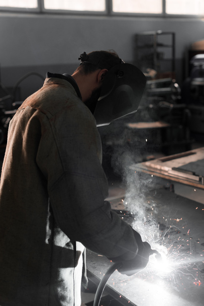 vista lateral de la fabricación de metal de soldadura trabajador con chispas en la fábrica
  - Foto, Imagen