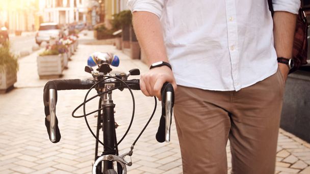 Closeup photo of young man walking on street with vintage bicycle at sunset - Foto, immagini