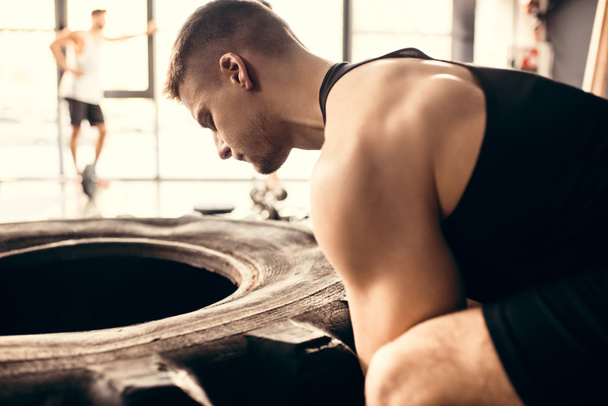 side view of muscular young sportsman exercising with tire in gym - Φωτογραφία, εικόνα