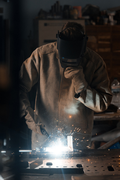 vista frontal del soldador en máscara de protección que trabaja con metal en fábrica
  - Foto, Imagen