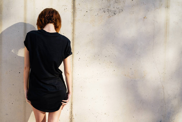 Attractive young woman wearing black blank t-shirt  posing against a background of a concrete wall - Photo, image