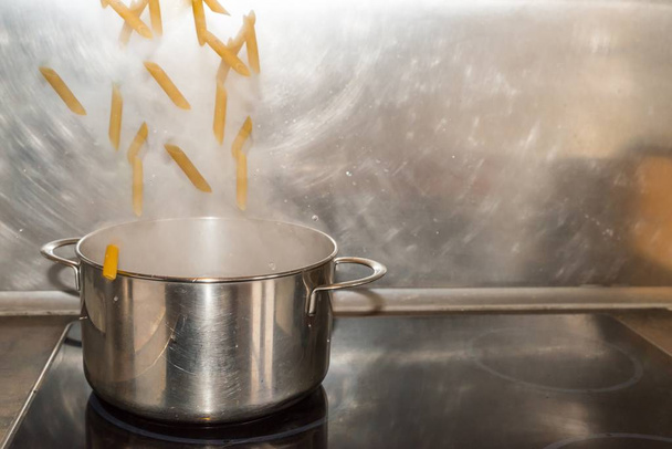 Penne Les nouilles rigides tombent dans une casserole avec de l'eau bouillante
 - Photo, image