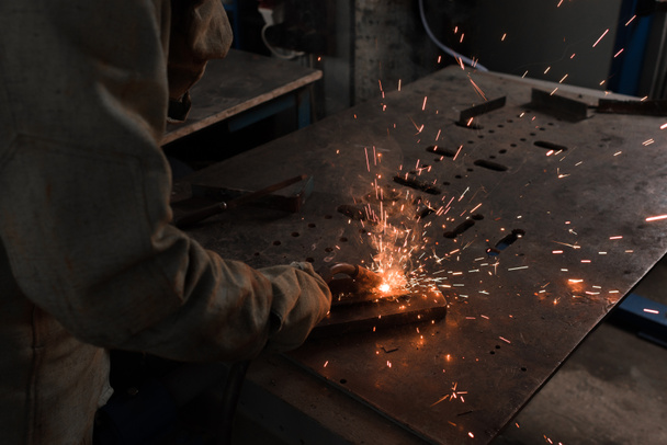 bijgesneden afbeelding van werknemer in bescherming masker lassen van metalen in fabriek  - Foto, afbeelding