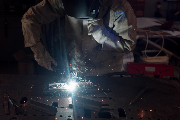 обрезанное изображение сварщика в защитной маске, работающей с металлом на заводе
  - Фото, изображение