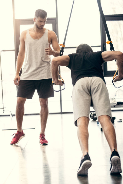 başparmak gösterilmesini ve direnç şeritli spor salonunda egzersiz sporcu bakarak eğitmen - Fotoğraf, Görsel