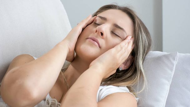 Close-up foto van vrouw met sterke hoofdpijn op de bank liggen en hand in hand op hoofd - Foto, afbeelding