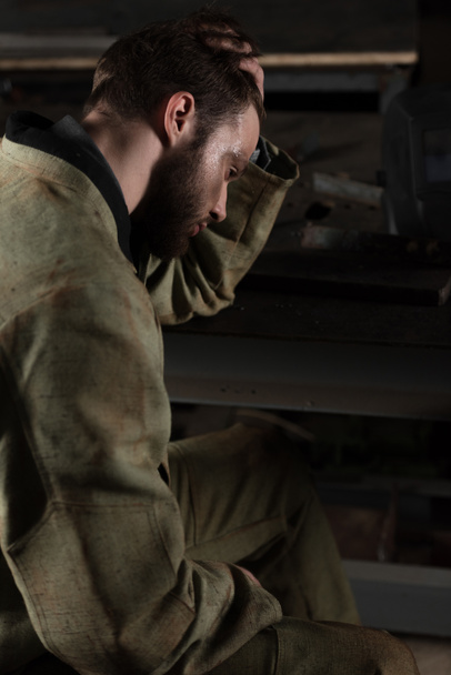 vista lateral de un joven trabajador masculino cansado sentado en la fábrica
  - Foto, imagen