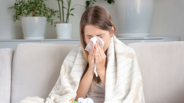 Retrato de una mujer enferma estornudando en papel sobre un sofá
 - Foto, Imagen