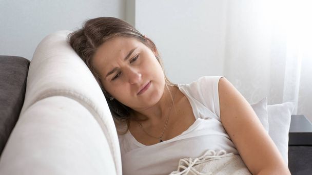Портрет хворої засмученої жінки, що сидить на дивані у вітальні
 - Фото, зображення