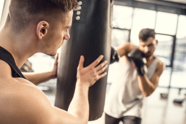 cropped shot of man holding punching bag while boxer hitting in gym - 写真・画像