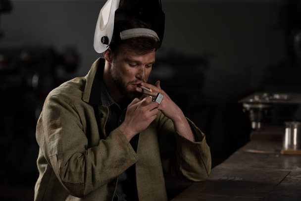 trabajador masculino con levantado máscara protectora cigarrillo relámpago en fábrica
 - Foto, imagen