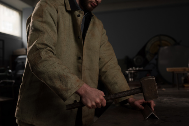 обрезанный снимок работника мужского пола, забивающего металлическую деталь на заводе
  - Фото, изображение