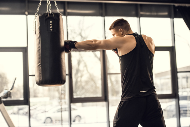 vista lateral del entrenamiento de boxeador joven muscular con saco de boxeo en el gimnasio
  - Foto, Imagen