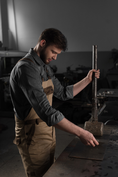 side view of young male worker hammering metal part at factory - Fotografie, Obrázek