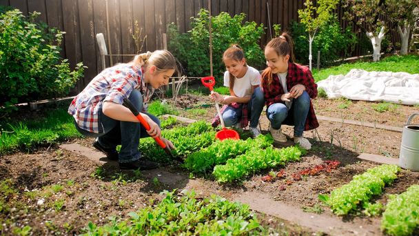 glückliche junge Frau mit Töchtern, die Samen in Garten pflanzen - Foto, Bild