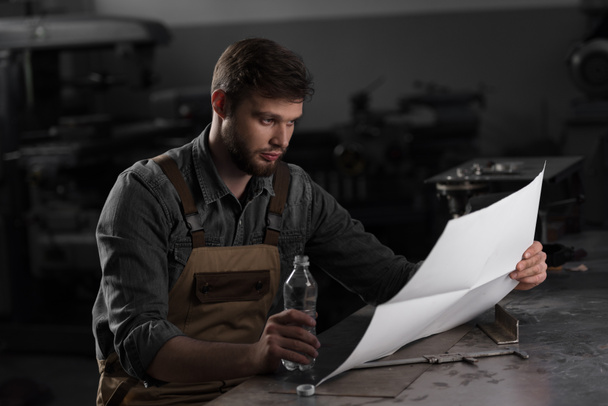 trabalhador sentado com garrafa de água e olhando para o modelo
  - Foto, Imagem