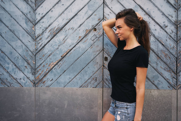 ライト ブルー木製フェンスに対して空白の黒 t シャツ立っての美しい若い女性 - 写真・画像