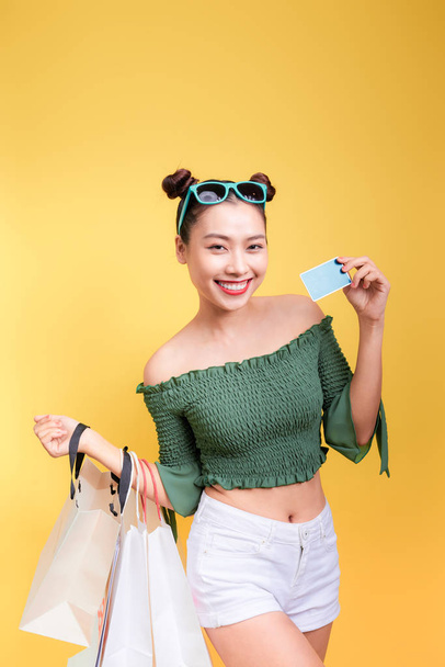 Compras mujer asiática sostiene bolsas de compras y una tarjeta de crédito sobre fondo amarillo
 - Foto, Imagen