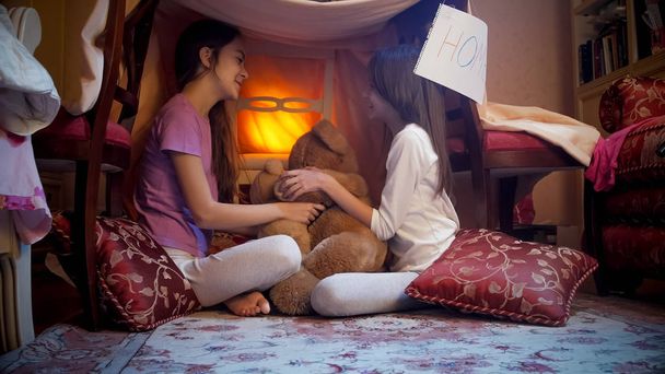 Two teenage girls sitting in tepee tent in bedroom at night - Photo, Image