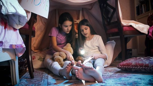 Duas meninas sentadas no chão à noite e lendo livro assustador
 - Foto, Imagem