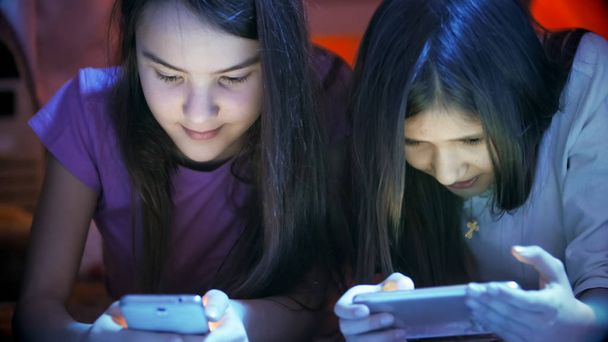 Retrato de cerca de dos chicas adolescentes con teléfonos móviles por la noche
 - Foto, Imagen