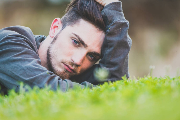Close-up portrait of a young man lying down a green garden. Man  - Photo, Image