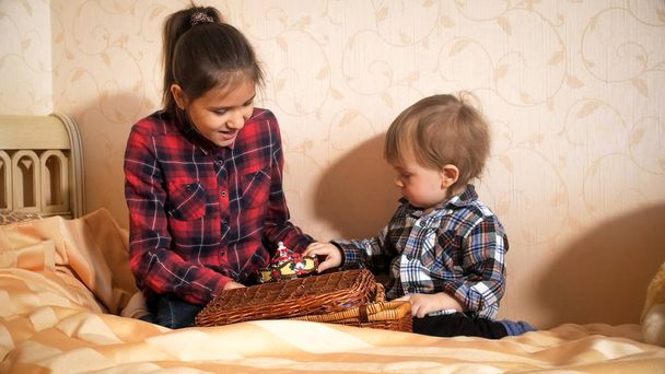 Cute toddler boy playing with elder sister on bed at bedroom - Photo, Image